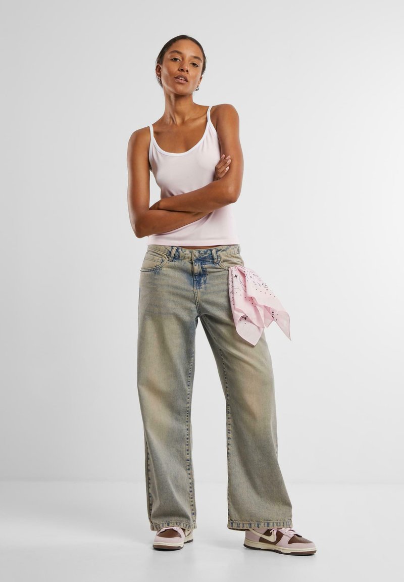 Lys rosa tank topp, løse falmede blå jeans med et rosa bandana knyttet i livet, og brune sneakers med rosa detaljer.