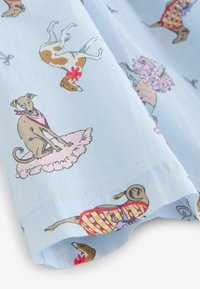 Svetlo modra tkanina z ilustracijami psov, ki nosijo pisane obleke in dodatke, vključno z roza tutu krili in rdečimi cvetovi.