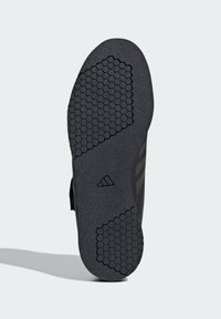 Sole di scarpa sportiva nera con motivo a esagoni, in materiale gommoso e tre strisce decorative. Presenta un logo Adidas al centro.