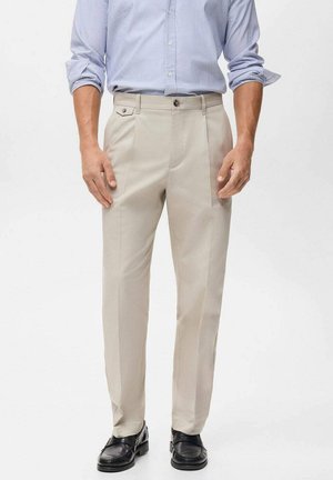 Beige tailored trousers with front pleats, side pockets, and a smooth fabric texture, paired with black leather shoes and a light blue striped shirt.