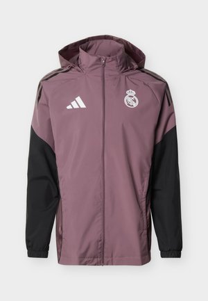 Lila-schwarze Sportjacke mit Reißverschluss und Kapuze, Adidas-Logo auf der rechten Brust und Real-Madrid-Wappen auf der linken Brust.