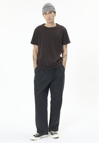 Tmavě hnědé tričko s krátkým rukávem, černé kalhoty, šedá pletená čepice a černé tenisky. Minimalistický design s volným střihem a postranními akcenty.