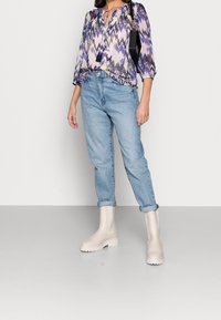 Blusa a fantasia multicolore con maniche a tre quarti, abbinata a jeans azzurri con risvolto e stivaletti beige. Inclusa una borsa nera.