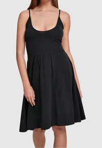 Svart ärmlös klänning med rundad halsringning, figursydd överdel och utsvängd kjol. Tillverkad av mjukt tyg med en slät yta.