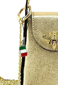 Gouden metallic handtas met een zwarte strap; voorzien van een zilveren charm met een mini Italiaanse vlag, versierd met een bij-embleem aan de voorkant.