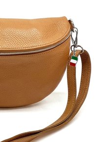 Tan leren schoudertas met een ronde vorm, zilveren ritssluiting en een bedel met de Italiaanse vlag die aan de schouderriem is bevestigd.