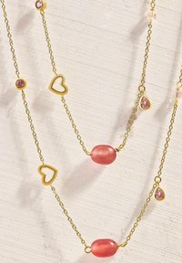 Collar de cadena en tono dorado con cuentas rosas, acentos en forma de corazón y pequeños detalles en forma de gema rosa. Varias capas crean profundidad y textura.