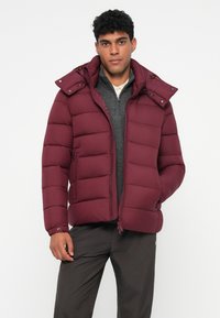Giacca imbottita bordeaux con cappuccio rimovibile, frontale con zip e tasche laterali. Presenta una texture trapuntata e polsini elastici.