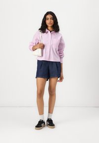 Rosa og hvite stripete skjorte med krage, blå denimshorts, svarte joggesko med hvite detaljer, og en liten hvit håndveske. Glatte teksturer.