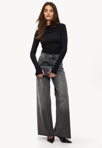 Zwarte lange mouw top met gedrapeerde halslijn, gecombineerd met hoog-getailleerde, wijde grijze jeans. Een zwarte handtas en puntige hakken maken de look compleet.