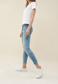 Vit kortärmad t-shirt i kombination med ljusblå skinny jeans, med en lätt urtvättad look och ankellång längd, bärs tillsammans med vita sneakers.