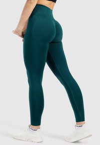 Legginsy w kolorze zielono-niebieskim, z wysokim stanem, wykonane z elastycznego materiału o gładkiej fakturze. Posiadają panele konturowe oraz dopasowany krój.