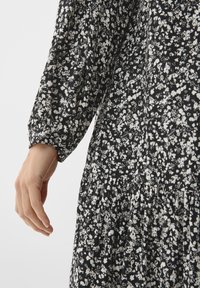 Schwarz-weißes Blumenkleid mit langen Ärmeln, geraffter Taille und einem fließenden Rock. Der Stoff hat ein strukturiertes Muster mit einer weichen Optik.