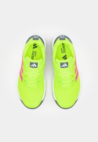 Neon gule sportssko med pink accenter, mesh-overdel, flade snørebånd og polstret krave. Har en holdbar gummisål og logo-detaljer.