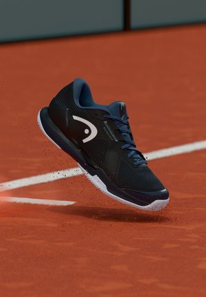 Zwarte sportschoen met bovenwerk van mesh, blauwe accenten en een wit logo. Voorzien van een profielzool voor grip op een kleibaan.