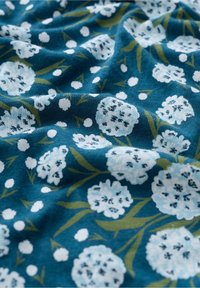 Květinová látka s tyrkysovým pozadím, obsahující světle modré květy a zelené listy. Měkký, strukturovaný materiál s rozptýlenými bílými tečkami.