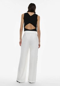 Top nero senza maniche con scollatura a forma di V sul retro, abbinato a pantaloni bianchi a vita alta e gamba larga, caratterizzati da una texture liscia e un design sartoriale.