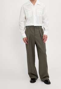 Vit långärmad skjorta med två bröstfickor, tillsammans med högmidjade, vida olivgröna byxor och svarta skor.