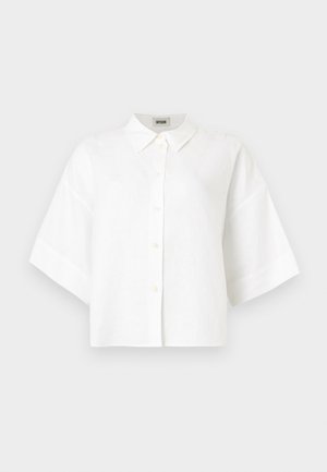 Valkoinen lyhythihainen kauluksellinen nappipaita, väljä malli ja sisäkauluksen näkyvä brändilaatta.