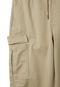 Pantalones cargo beige con una tela texturizada. Presenta un bolsillo lateral y detalles de costura. Cintura elástica con cordón.