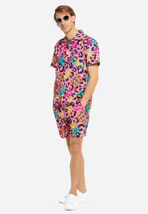 Short-sleeve, pink shirt and matching shorts featuring a bold, colorful pattern with eyes, bananas, and abstract designs. White sneakers.