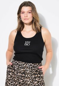 Camiseta de tirantes negra con el texto "STUDIO" impreso en la parte delantera, combinada con pantalones de leopardo que tienen bolsillos y una cintura elástica.