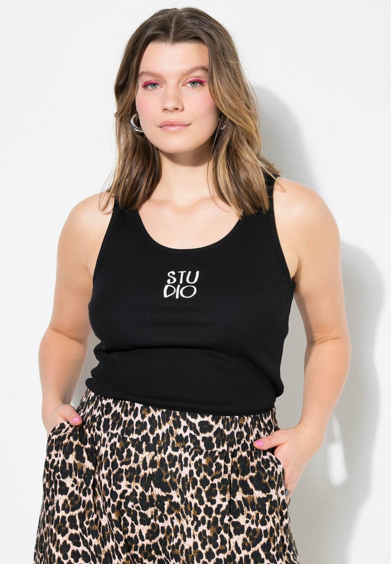 Camiseta de tirantes negra con el texto "STUDIO" impreso en la parte delantera, combinada con pantalones de leopardo que tienen bolsillos y una cintura elástica.