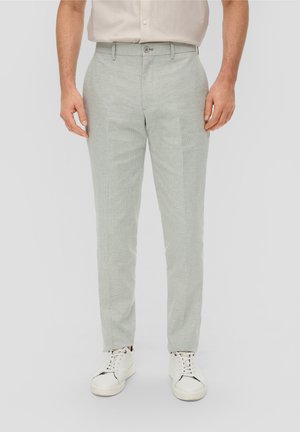Hellgrüne gemusterte Hose mit taillierter Passform, ausgestattet mit einem Knopfverschluss und Taschen, kombiniert mit weißen Sneakers. Glatte Textur.
