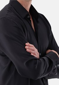 Zwarte blouse met lange mouwen, een gladde textuur, klassieke kraag en knoopmanchetten, voorzien van zwarte knopen en een ontspannen pasvorm.