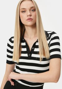 Svart och vit randig ribbad polo med korta ärmar och krage, som har två silvriga knappar vid halsen.