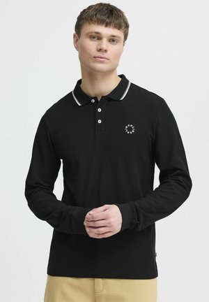 Polo negro de manga larga con ribete blanco en el cuello, tapeta de tres botones y un pequeño logo en el lado izquierdo del pecho. Textura suave.