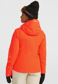 Felroze geïsoleerde jas met een capuchon en zwarte accenten, met een gladde textuur. Draagt een zwarte beanie en handschoenen.