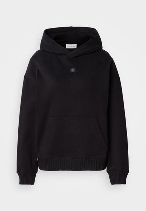 Mustan puuvillahoodie, kus on ees tasku, ribbetud varrukad ja alläär, ning rinnas väike brändimärk.