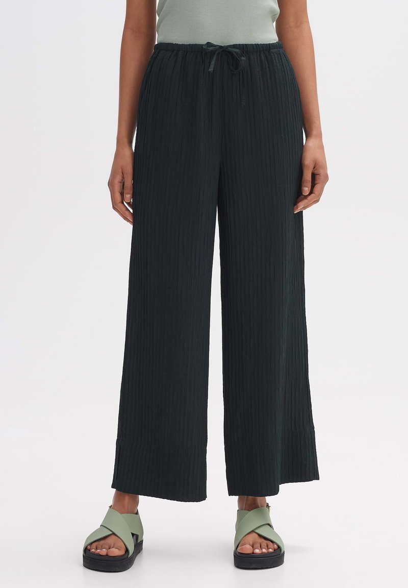 Wijde, donkergroene broek met een gestructureerde stof en een koordtaille. Draag het met lichtgroene sandalen met een dikke zool en gekruiste banden.