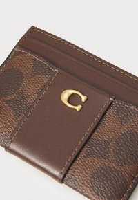 Bruine leren kaart houder met een textuur ontwerp, gouden hardware logo en meerdere kaartslots met contrasterende stiksels.