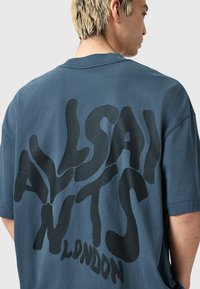 Camiseta de algodón azul con un gran texto gráfico negro en la parte posterior, cuello redondo y mangas cortas; diseño de corte relajado.