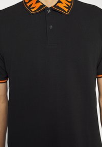 Polo noir à manches courtes avec deux boutons noirs, avec un col à motif orange et noir et une finition orange sur les bords des manches.