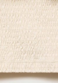 Tessuto color crema con una superficie testurizzata caratterizzato da pieghe arricciate. Il materiale è morbido, con cuciture visibili che mettono in risalto il design.
