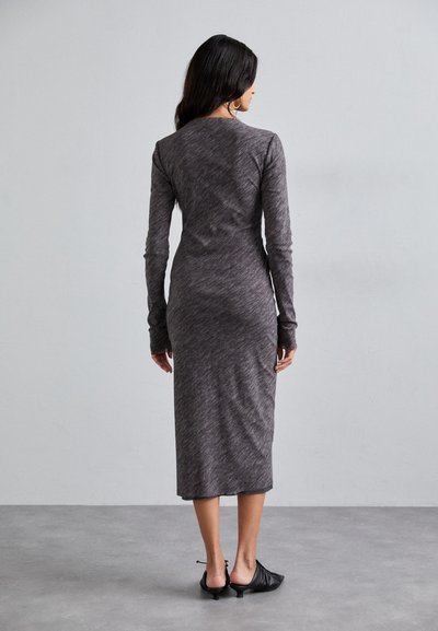 Gray long-sleeve dress with a bodycon fit, made from a textured fabric, reaching mid-calf. Paired with black, open-toe shoes.