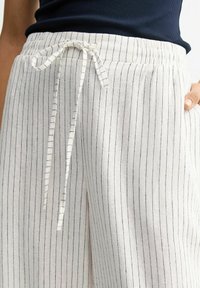 Witte gestreepte broek met een trekkoord in de taille, gemaakt van een licht materiaal met subtiele zwarte verticale lijnen en een relaxte pasvorm.
