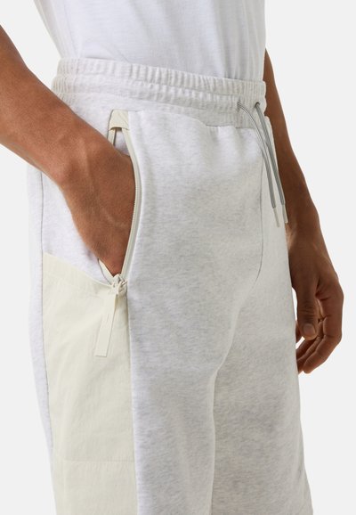 Lichtgrijze sweatpants met een gladde textuur, voorzien van een wit stoffen patchzakje en een zijrits, elastische tailleband met trekkoorden.