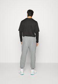 Černé tričko s krátkým rukávem a texturovaným detailem, šedé zúžené kalhoty a bílé tenisky s jemnými modrými akcenty. Pohled zezadu.