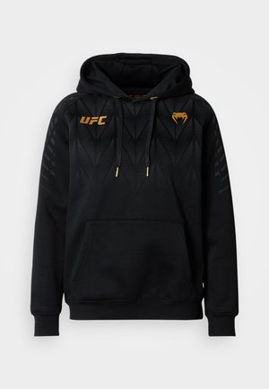 Crna majica s kapuljačom s teksturiranim trokutastim uzorkom, zlatnim detaljima, džepom tipa kengur i podesivim vezicama. Prikazuje UFC logo.