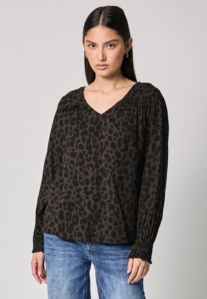 Blouse noire avec imprimé léopard, décolleté en V, détails plissés aux épaules, manches longues avec poignets froncés, portée avec un jean bleu.