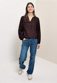 Chemisier marron à boutons avec des manches longues, associé à un jean flare bleu et des baskets blanches. Design simple, tissu doux, accents minimaux.