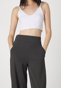 Top corto blanco combinado con pantalones de tiro alto de color gris oscuro que cuentan con bolsillos laterales y un corte relajado y suave.