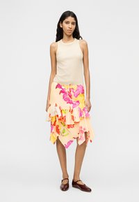 Haut sans manches beige associé à une jupe fleurie multicolore avec volants et ourlet asymétrique, porté avec des chaussures marron foncé.