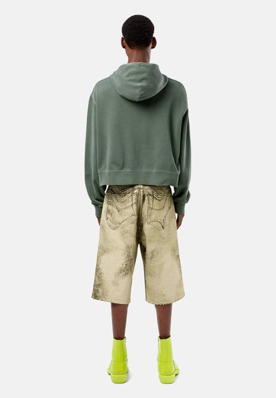 Groene cropped hoodie, beige versleten shorts met geprinte zakdetails, en neon groene enkellaarzen. Minimalistisch ontwerp met zachte texturen.