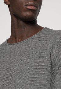 Maglione grigio con texture, dal collo rotondo, caratterizzato da un sottile motivo a spina di pesce e bordi a costine, con una consistenza di spessore medio.