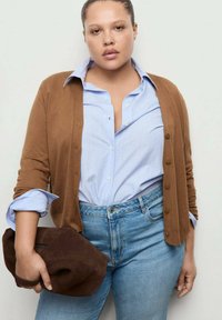 Bruine cardigan over een blauw-wit gestreept overhemd met knoopjes, gecombineerd met spijkerbroek. De outfit wordt aangevuld met een bruine suède clutch. Simpel ontwerp, casual stijl.